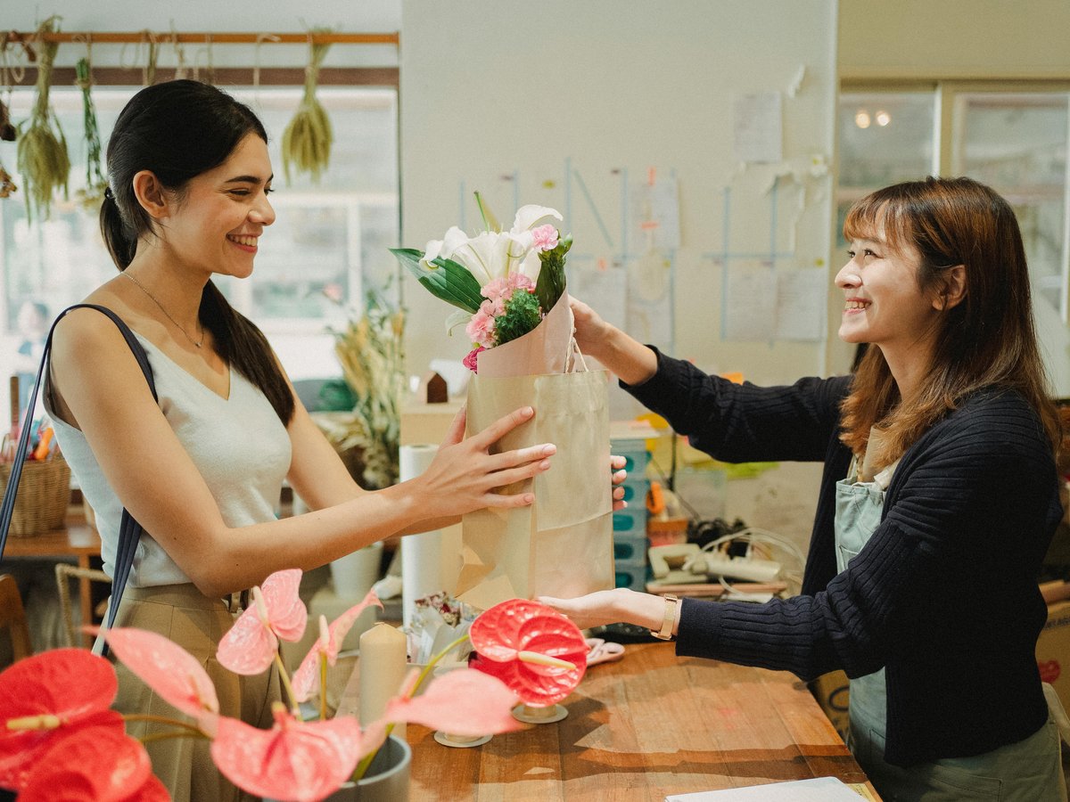 花屋の店員が外国人のお客様に笑顔で商品を手渡している様子